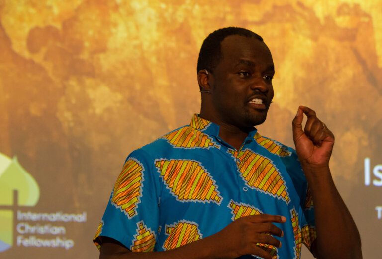 Adult man wearing a colorful shirt and headset microphone gesturing with one hand as he speaks intensely