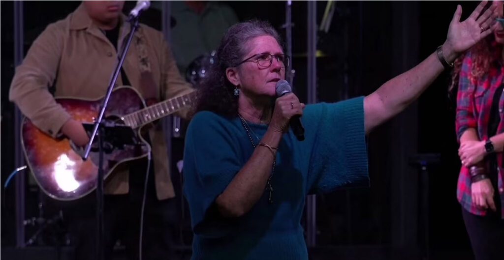 Older woman gesturing with arm raised speaking into a microphone